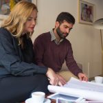 A man and woman sit on a couch, examining a blueprint together with focused expressions