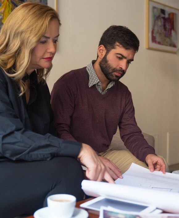 A man and woman sit on a couch, examining a blueprint together with focused expressions