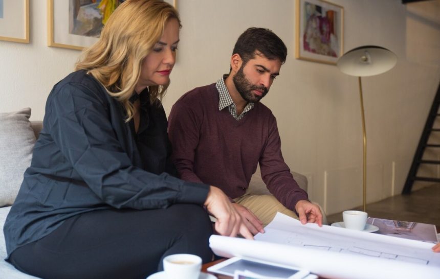 A man and woman sit on a couch, examining a blueprint together with focused expressions
